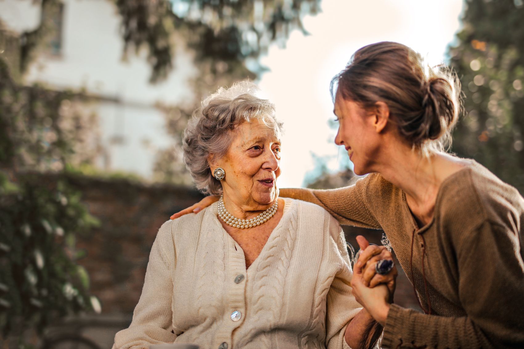 An adult daughter holding her elderly mother's hand and smiling together in a garden
